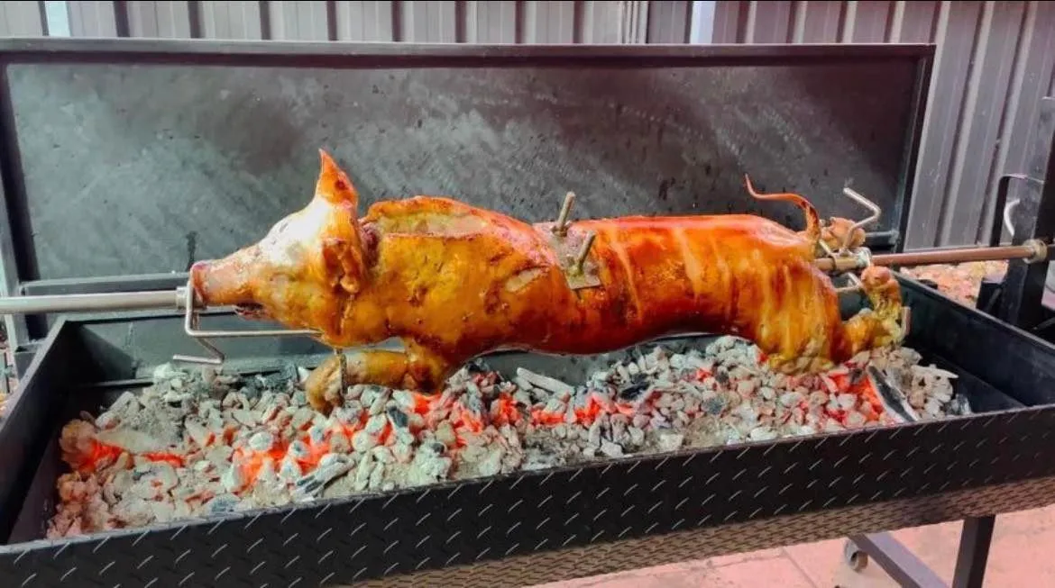 Whole pig cooking on a hired spit roast rig over charcoal in Adelaide